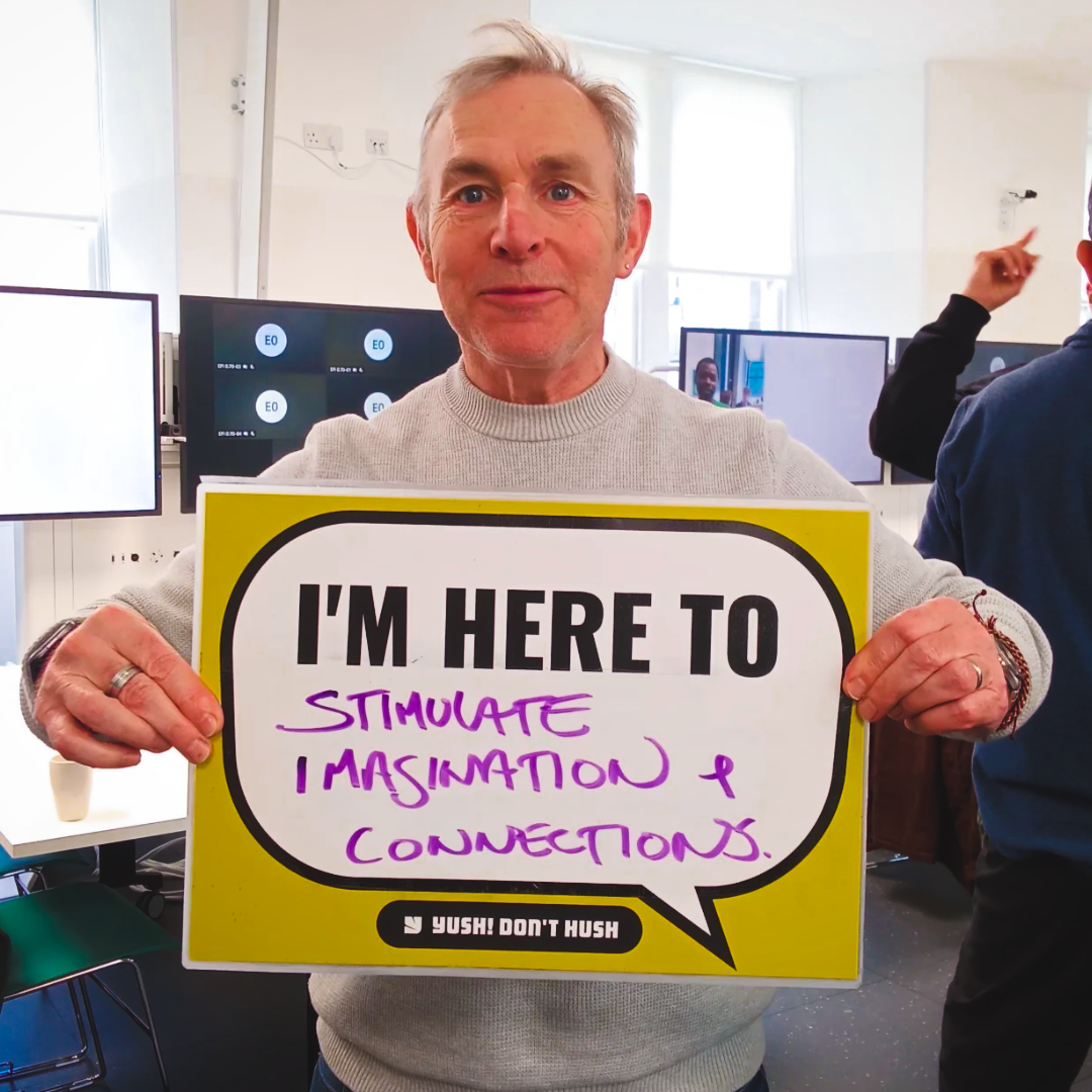 Man at EFI holding a yellow YUSH sign reading I'm here to stimulate imagination and connections