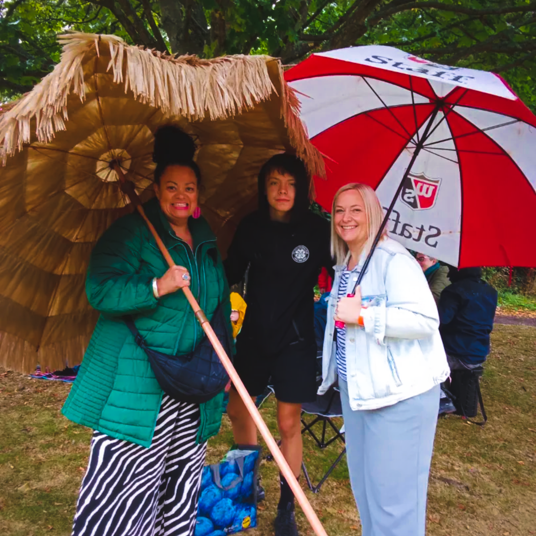 Three people under umbrellas at a multicultural community festival